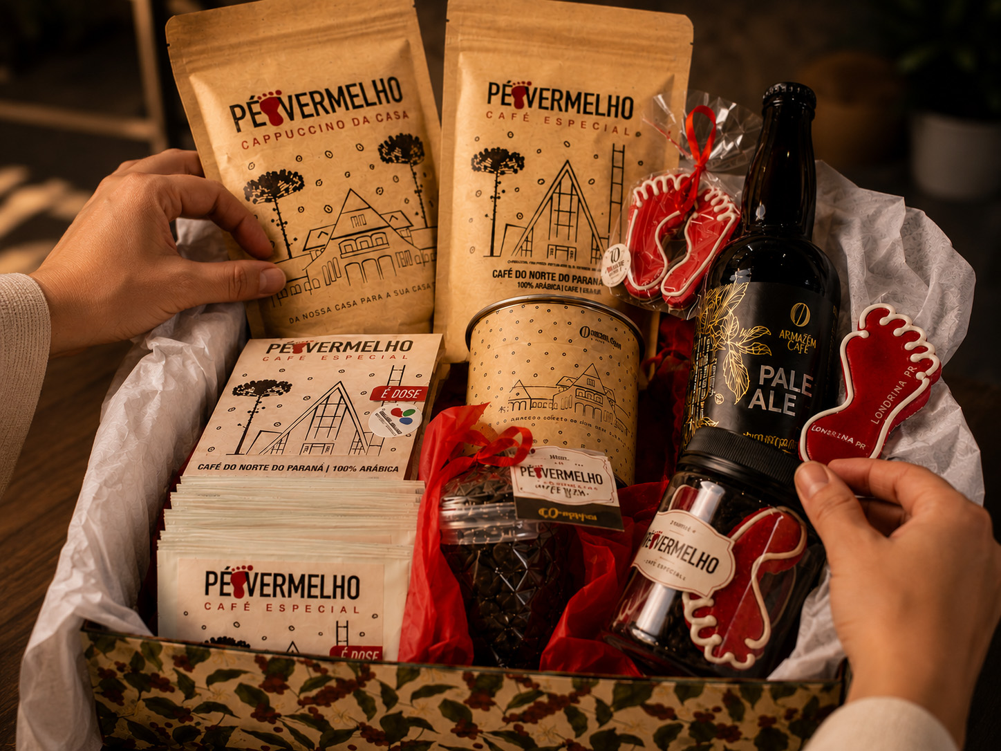 Mãos montando um kit Pé Vermelho com cafés especiais, sachês, biscoitos pé-vermelho e Pale Ale+Café